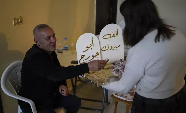 A woman distributes sweets to celebrate the return of Suheil Hamwi, who spent 32 years in prison in Syria and returned to Lebanon after the government of Bashar Assad was toppled, inside of his home in Chekka, Lebanon, Tuesday, Dec. 10, 2024. (AP Photo/Hassan Ammar)