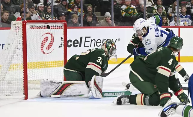 Vancouver Canucks left wing Jake DeBrusk, right, hits the puck past Minnesota Wild goalie Filip Gustavsson during the second period of an NHL hockey game Tuesday, Dec. 3, 2024, in St. Paul, Minn. (AP Photo/Craig Lassig)