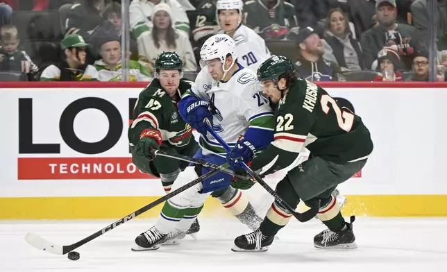 Vancouver Canucks left wing Nils Hoglander, center, battles for control of the puck with Minnesota Wild center Marat Khusnutdinov (22) and defenseman Declan Chisholm during the second period of an NHL hockey game Tuesday, Dec. 3, 2024, in St. Paul, Minn. (AP Photo/Craig Lassig)