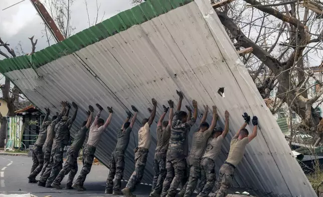 This photo provided by the French Army shows soldiers lifting a collapsed barrier in the Indian Ocean French territory of Mayotte, Wednesday Dec.18, 2024, as the cyclone on Saturday was the deadliest storm to strike the territory in nearly a century. (D Piatacrrea, Etat Major des Armees/Legion Etrangere via AP)