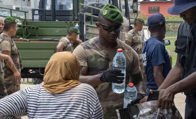 This photo provided by the French Army shows a soldier giving a bottle of water to a resident in the Indian Ocean French territory of Mayotte, Wednesday Dec.18, 2024, as the cyclone on Saturday was the deadliest storm to strike the territory in nearly a century. (D Piatacrrea, Etat Major des Armees/Legion Etrangere via AP)