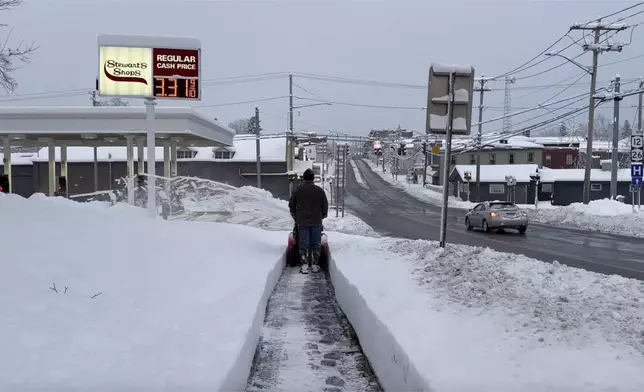 A person clears the snow from the sidewalk in Lowville, N.Y., on Saturday, Nov. 30, 2024. (AP Photo/Cara Anna)