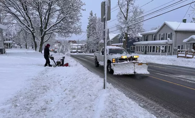 A person clears the snow from the sidewalk in Lowville, N.Y., on Saturday, Nov. 30, 2024. (AP Photo/Cara Anna)