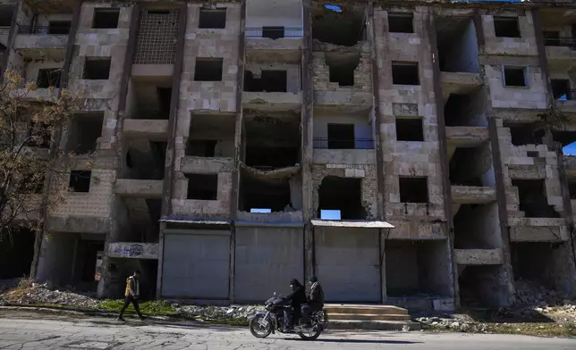 People walk by a destroyed residential building in the Masaken Hanano district in Aleppo, Syria, on Saturday, Dec. 14, 2024. (AP Photo/Khalil Hamra)