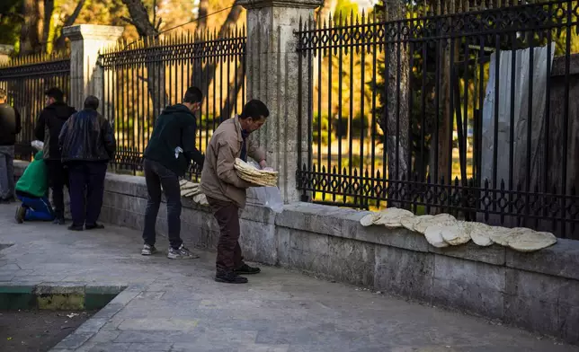 Local residents fill plastic bags with bread they bought from a bakery in Aleppo, Syria, on Saturday, Dec. 14, 2024. (AP Photo/Khalil Hamra)