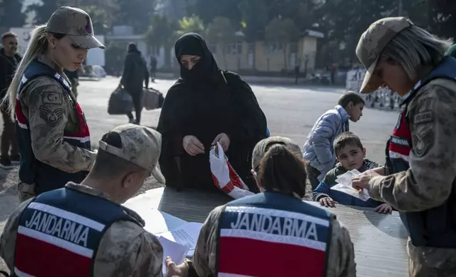 A Syrian woman gives her documents to Turkish gendarmes while crossing into Syria from Turkey at the Cilvegozu border gate near Antakya, southern Turkey, on Tuesday, Dec. 10, 2024. (AP Photo/Metin Yoksu)