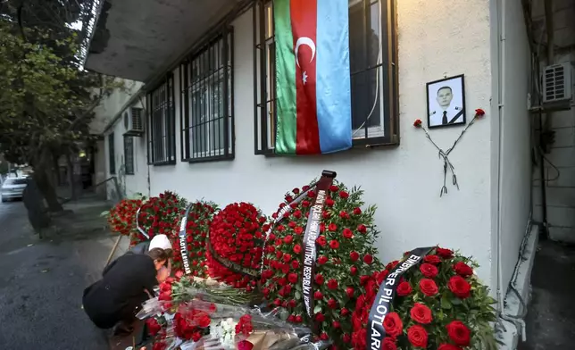 An Azerbaijan national flag, flowers and candles are seen at the wall of the apartment building in memory of a pilot Alexander Kalyanina, one of victims who died in the Azerbaijan Airlines Embraer 190 crash near the Kazakhstan's airport of Aktau, in Baku, Azerbaijan, on Saturday, Dec. 28, 2024. (AP Photo)