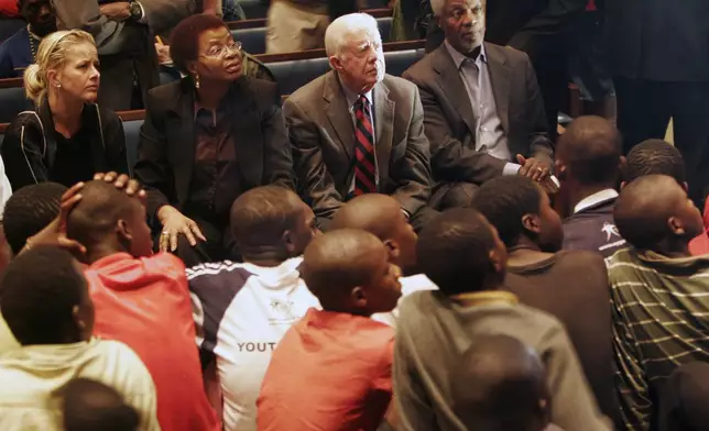 FILE - Former U.S. President Jimmy Carter, background second right, former U.N. head Kofi Annan, background right, and Graca Machel, the wife of former South African President Nelson Mandela, background second from left, watch children perform during a visit to the Central Methodist Church in Johannesburg, South Africa, Nov. 23, 2008. The diplomats were barred entry into Zimbabwe on a humanitarian visit over the weekend. (AP Photo/Denis Farrell, File)