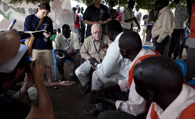 FILE - Former U.S. President Jimmy Carter, center, speaks with journalists and voting station authorities outside a polling station near Juba, southern Sudan, April 13, 2010. (AP Photo/Pete Muller, File)