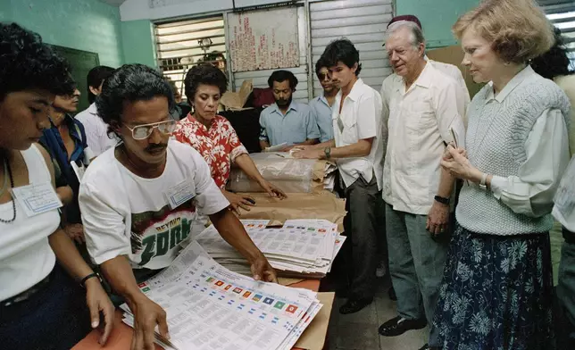 FILE - Former U.S. President Jimmy Carter and his wife, Rosalynn, right, watch election workers prepare ballots at a polling station in Managua, Nicaragua, Feb. 25, 1990. (AP Photo/J. Scott Applewhite, File)