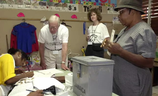 FILE - Former U.S. President Jimmy Carter, second left, and Jennifer McCoy, third left, observe the voting process, while Joyce Grey, right, waits to cast her ballot at a polling station in Kingston, Jamaica, Oct. 16, 2002. (AP Photo/Andres Leighton, File)