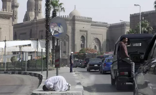 FILE - The motorcade of former U.S. President Jimmy Carter passes a man praying in the street beneath an election poster for presidential candidate Khaled Ali during the election of a new president after the fall of ex-President Hosni Mubarak in Cairo, May 23, 2012. (AP Photo/Thomas Hartwell, File)