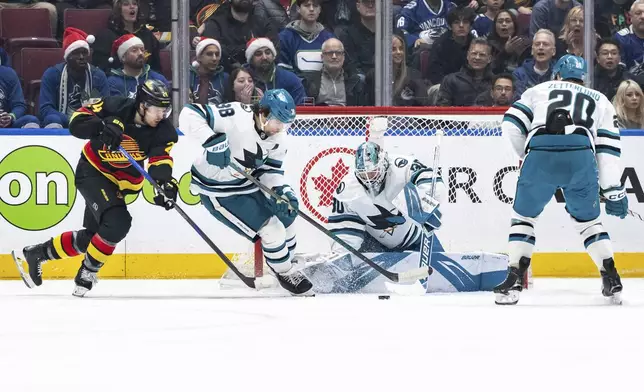 San Jose Sharks goaltender Yaroslav Askarov (30) stops the puck as teammate Mario Ferraro (38) and Vancouver Canucks' Pius Suter (24) watch during first-period NHL hockey game action in Vancouver, British Columbia, Monday, Dec. 23, 2024. (Ethan Cairns/The Canadian Press via AP)