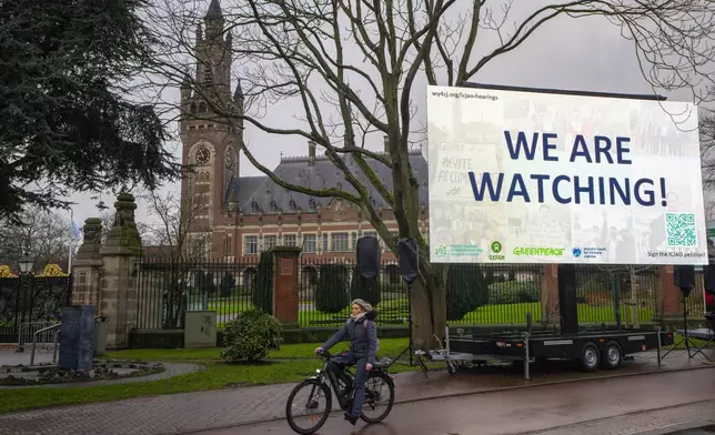 Activists put up a billboard outside the International Court of Justice, in The Hague, Netherlands, as it opens hearings into what countries worldwide are legally required to do to combat climate change and help vulnerable nations fight its devastating impact, Monday, Dec. 2, 2024. (AP Photo/Peter Dejong)