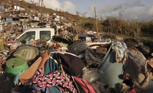 A woman carrying her belongings walks past debris after Cyclone Chido in the Kaweni slum Thursday, Dec. 19, 2024, on the outskirts of Mamoudzou, in the French Indian Ocean island of Mayotte. (AP Photo/Adrienne Surprenant)