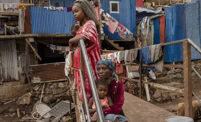 Women rest on a footbridge over a stream filled with debris in the Kaweni slum in the French Indian Ocean island of Mayotte, Thursday, Dec. 19, 2024, after Cyclone Chido. (AP Photo/Adrienne Surprenant)