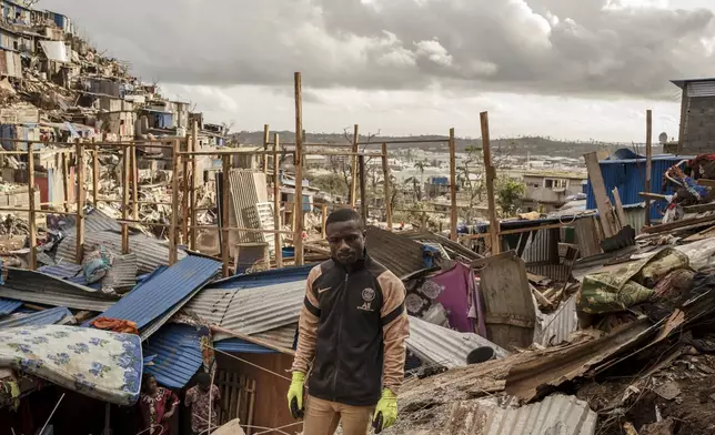 Nassirou Hamidouni, 28, father of five, stands amongst the debris of the neighboring destroyed home in the slum of Kaweni on the outskirts of Mamoudzou, in the French Indian Ocean island of Mayotte Thursday, Dec. 19, 2024, after Cyclone Chido. (AP Photo/Adrienne Surprenant)