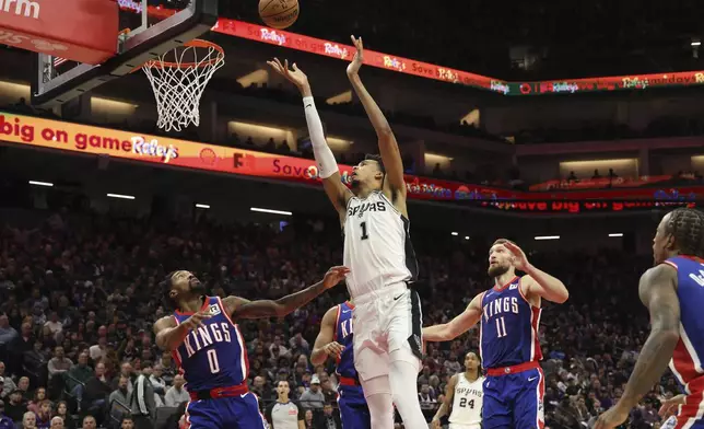 San Antonio Spurs center Victor Wembanyama (1) shoots against Sacramento Kings guard Malik Monk (0) and forward Domantas Sabonis (11) during the second half of an NBA basketball game in Sacramento, Calif., Sunday, Dec. 1, 2024. (AP Photo/Jed Jacobsohn)