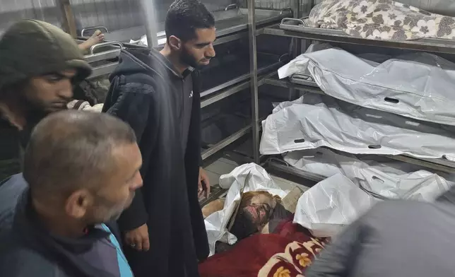 Palestinians stand next to bodies of people killed in an Israeli airstrike in Muwasi, after they were brought to the morgue of a hospital in Khan Younis, Gaza Strip, Wednesday, Dec. 4, 2024. (AP Photo/Mohammad Jahjouh)