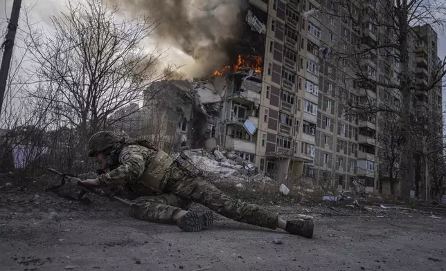 FILE - A Ukrainian police officer takes cover in front of a burning building that was hit in a Russian airstrike in Avdiivka, Ukraine, Friday, March 17, 2023. (AP Photo/Evgeniy Maloletka, File)