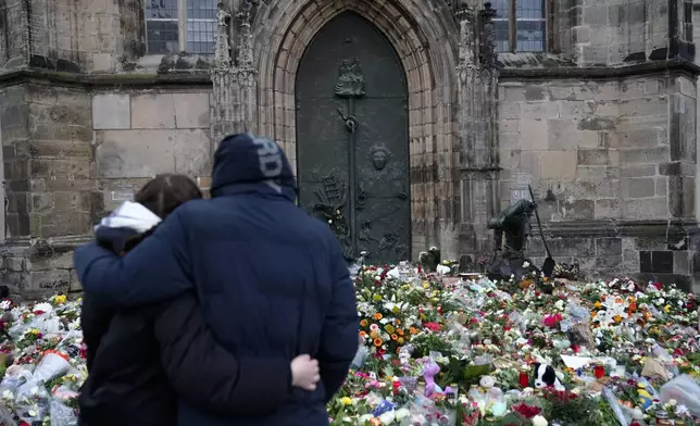 A couple embrace each other in front of flowers and candles laid down at the Johannis church close to the Christmas market, where a car drove into a crowd on Friday evening, in Magdeburg, Germany, Sunday, Dec. 22, 2024. (AP Photo/Ebrahim Noroozi)