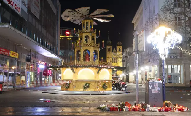 Candles and flowers sit in front of the Christmas market early Sunday, Dec. 22, 2024, in Magdeburg, Germany, after a car drove into a crowd at the market on Friday, Dec. 20. (Sebastian Kahnert/dpa via AP)