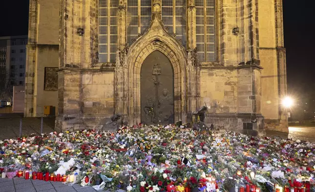 Candles, flowers and wreaths sit in front of the entrance to St. John's Church early Sunday, Dec. 22, 2024, in Magdeburg, Germany, after a car drove into a crowd at a Christmas market on Friday, Dec. 20. (Sebastian Kahnert/dpa via AP)