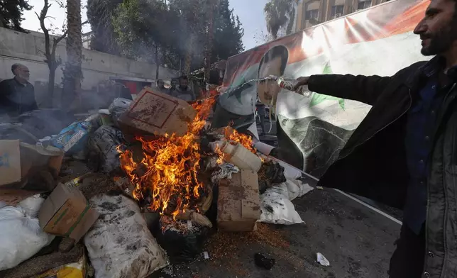 A banner with an image depicting the ousted Syrian President Bashar Assad is placed on the fire as a Syrian member of the rebel forces destroys drugs and alcoholic beverages, found at a complex building, in Damascus, Syria, Wednesday, Dec. 25, 2024. (AP Photo/Omar Sanadiki)