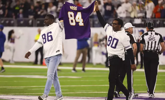 Formers Minnesota Vikings players Jake Reed, left, and Cris Carter carry a jersey for former Vikings wide receiver Randy Moss before an NFL football game against the Chicago Bears, Monday, Dec. 16, 2024, in Minneapolis. (AP Photo/Bruce Kluckhohn)