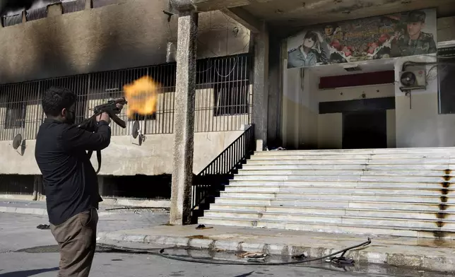 FILE.- A Syrian fighter from rebel group, fires towards a poster at the entrance of the notorious security detention centre called Palestine Branch, which pictures the late Syrian President Hafez Assad and his son the ouster Syrian president Bashar Assad, in Damascus, Syria, Saturday, Dec. 14, 2024. (AP Photo/Hussein Malla,File)