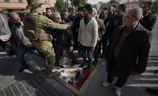 FILE.- A Syrian fighter, left, stands guard as members of ousted Syrian President Bashar Assad's army step on his portrait as a sign of disdain, lining up before they register their names with Syrian rebels as part of an "identification and reconciliation process" in Damascus, Syria, Monday, Dec. 23, 2024. (AP Photo/Hussein Malla,File)