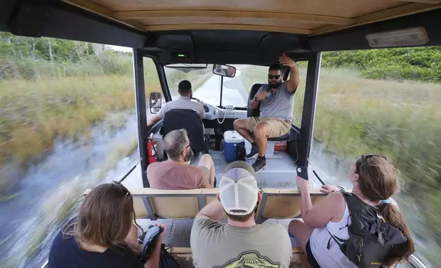 Naturalist tour guide Richard Petrosky speaks to visitors as fellow guide Juan Macias steers the tram through several inches of water covering long stretches of the path in the Shark Valley area of Florida's Everglades National Park, Fla., Wednesday, Nov. 20, 2024. (AP Photo/Rebecca Blackwell)