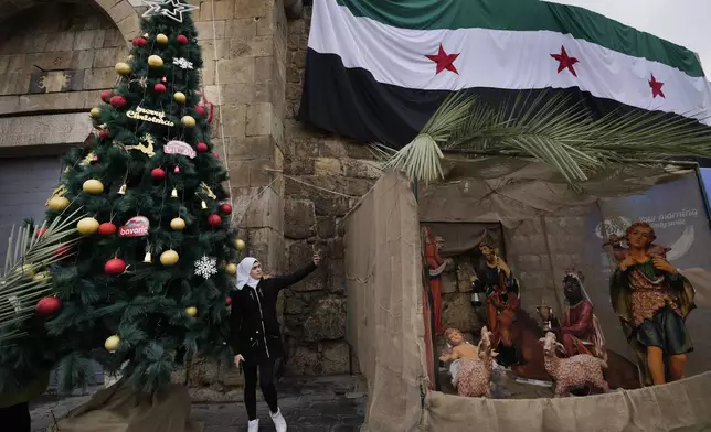 A Syrian Muslim woman takes a selfie in front of a Christmas tree in Bab Touma neighbourhood, in Damascus, Syria, Tuesday, Dec. 24, 2024. (AP Photo/Hussein Malla)