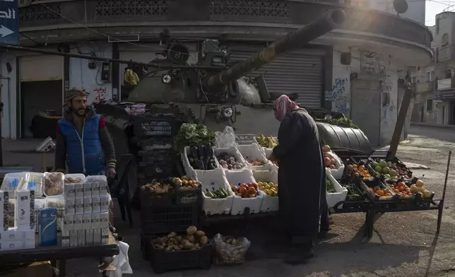 A man looks at fruits and vegetables displayed for sale in front of an ousted Syrian government forces tank that was left on a street in an Alawite neighbourhood, in Homs, Syria, Thursday, Dec. 26, 2024. (AP Photo/Leo Correa)