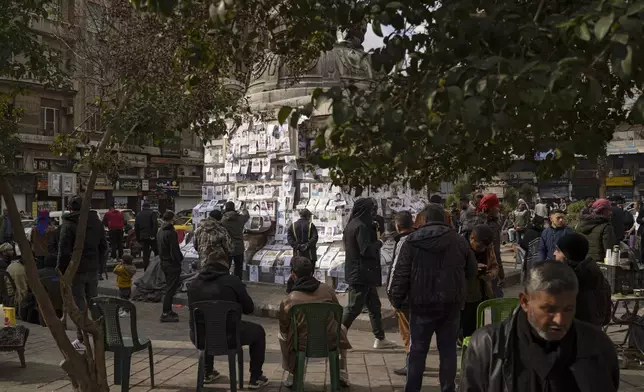 People look at photos of people reported to be missing, by members of ousted Syrian President Bashar Assad's army or a pro-government militia, as others sit to smoke and drink tea at the Marjeh square in Damascus, Syria, Sunday, Dec. 22, 2024. (AP Photo/Leo Correa)