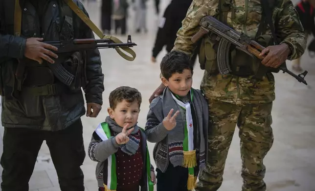 Two boys have their picture taken posing with Syrian fighters at the Umayyad Mosque ahead of Friday prayers in Damascus, Syria, Friday Dec. 20, 2024. 2024.(AP Photo/Leo Correa)