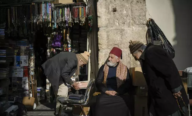 A man sits next to a vendor setting up his shop in the Old City , near the Umayyad Mosque, ahead of Friday prayers in Damascus, Syria, Friday, Dec. 20, 2024. (AP Photo/Leo Correa)