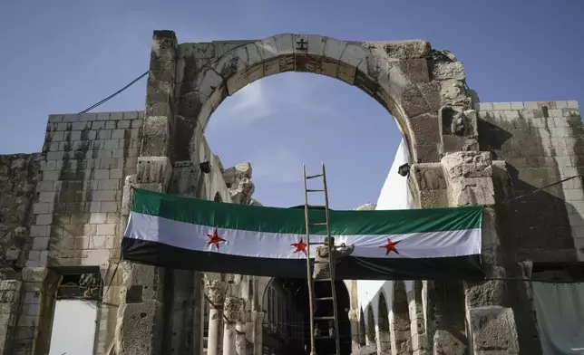 A worker sets up a Syrian "revolutionary" flag at the entrance of the Umayyad Mosque ahead of Friday prayers in Damascus, Syria, Friday Dec. 20, 2024. 2024.(AP Photo/Leo Correa)