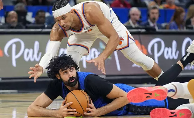 Orlando Magic center Goga Bitadze, lower left, tries to pass after collecting a loose ball in front of New York Knicks guard Josh Hart during the second half of an NBA basketball game, Friday, Dec. 27, 2024, in Orlando, Fla. (AP Photo/John Raoux)