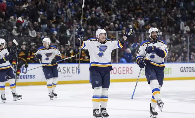 St. Louis Blues' Jake Neighbours, centre, and Pierre-Olivier Joseph, right, celebrate Dylan Holloway's winning goal against the Vancouver Canucks during overtime during an NHL hockey game in Vancouver, Tuesday, Dec. 10, 2024. (Darryl Dyck/The Canadian Press via AP)