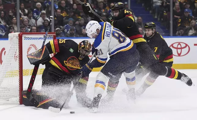 Vancouver Canucks goalie Thatcher Demko (35) stops St. Louis Blues' Dylan Holloway (81) as Vancouver's Noah Juulsen (47) checks him during the second period of an NHL hockey game, Tuesday, Dec. 10, 2024 in Vancouver, British Columbia. (Darryl Dyck/The Canadian Press via AP)