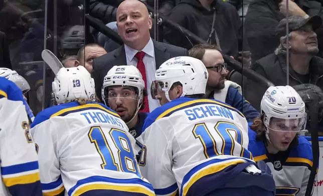 St. Louis Blues head coach Jim Montgomery, back, stands on the bench as Jordan Kyrou (25) talks to Robert Thomas (18) and Brayden Schenn (10) while Oskar Sundqvist (70) looks on during the second period of an NHL hockey game against the Vancouver Canucks in Vancouver Tuesday, Dec. 10, 2024. (Darryl Dyck/The Canadian Press via AP)