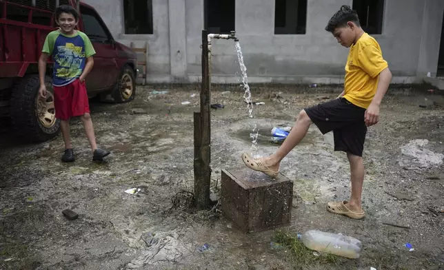 A youth rinses off his shoe in the Lempira settlement, situated next to Los Pinares iron oxide mining project, in Tocoa, Honduras, Saturday, Dec. 7, 2024. (AP Photo/Moises Castillo)