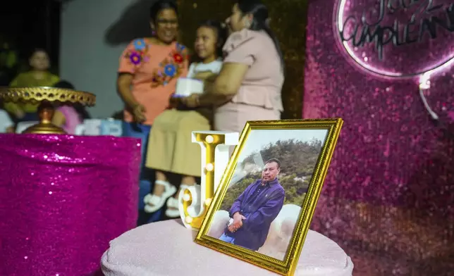 A portrait of slain environmentalist Juan López sits on a table as his daughter Julia Lopez Peña poses for a photo with relatives, at her ninth birthday party, at the family home in Tocoa, Honduras, Saturday, Dec. 7, 2024. (AP Photo/Moises Castillo)