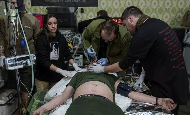 A medic treats an injured Ukrainian serviceman at Medical Service "Ulf" of the 108th Separate Battalion "Da Vinci Wolves" on Pokrovsk direction, Ukraine, Monday, Dec. 23, 2024. (AP Photo/Evgeniy Maloletka)