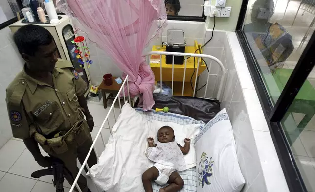 FILE- A Sri Lankan policeman guards the tsunami survivor infant dubbed "Baby 81" inside a ward as people watch from outside at a hospital in Kalmunai, about 210 kilometers (131 miles) east of Colombo, Sri Lanka, Feb. 3, 2005. (AP Photo/Rafiq Maqbool, File)