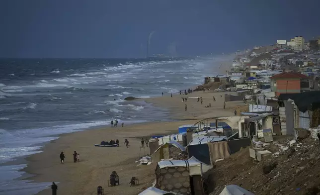 People walk along the beach next to a tent refugee camp for displaced Palestinians in Deir al-Balah, central Gaza Strip, Monday, Dec .30, 2024. (AP Photo/Abdel Kareem Hana)