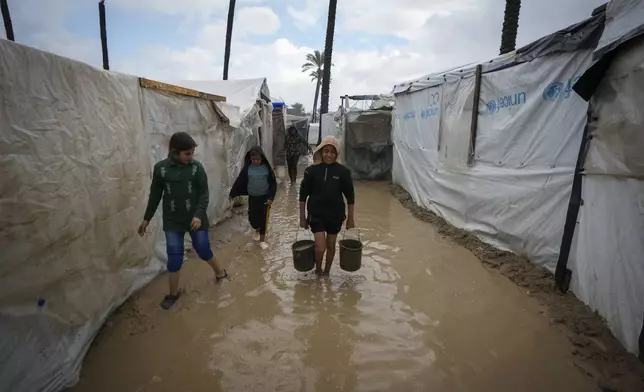 Palestinian children carry buckets of water after overnight rainfall at the refugee tent camp for displaced Palestinians in Deir al-Balah, central Gaza Strip, Tuesday, Dec. 31, 2024. (AP Photo/Abdel Kareem Hana)