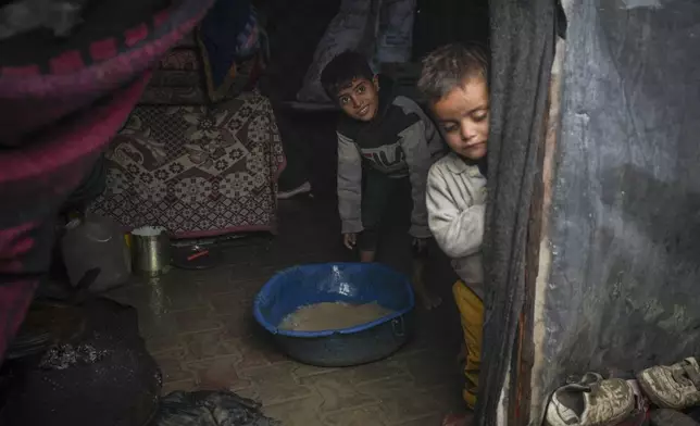 Brothers Belal, 5, and Mohammed Hamad, 7, collect water from their flooded family tent after overnight rainfall at the refugee tent camp for displaced Palestinians in Deir al-Balah, central Gaza Strip, Tuesday, Dec. 31, 2024. (AP Photo/Abdel Kareem Hana)