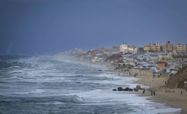 People walk along the beach next to a tent refugee camp for displaced Palestinians in Deir al-Balah, central Gaza Strip, Monday, Dec .30, 2024. (AP Photo/Abdel Kareem Hana)